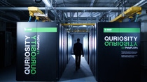 Blick in ein Rechenzentrum: Eine Person geht durch einen beleuchteten Gang zwischen Reihen schwarzer Server-Racks des BASF-Supercomputers „Quriosity“.