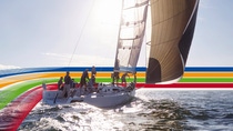 People on a sailing boat in the ocean, under a bright sky, surrounded by a key visual of four lines in blue, orange, green and red (photoshopped)