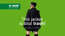 A woman wearing a black jacket against green background. The text reads: "This jacket is total trash!"
