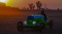 A man sitting in an electric vehicle on a field by sunset. A man sitting in an electric vehicle on a field by sunset.