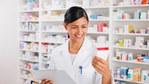 Pharmacist in drug store holding clipboard reading medication box