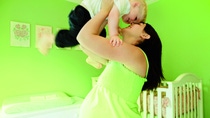 Pregnant woman lifting son (2-4) in air in nursery, smiling, side view