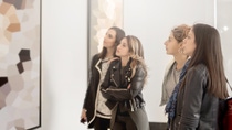 Four girl friends looking at modern painting in art gallery. Abstract painting