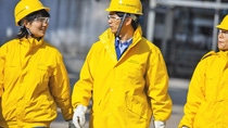 这张图片是巴斯夫生产基地中的三名工人，他们身穿黄色户外服，头戴黄色安全帽。 