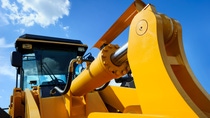 Bulldozer, huge yellow powerful construction machine with big scoop, focused on hydraulic piston arm, heavy industry, blue sky and white clouds on background Bulldozer, huge yellow powerful construction machine with big scoop, focused on hydraulic piston arm, heavy industry, blue sky and white clouds on background