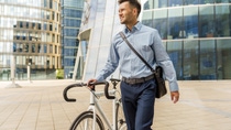 Male in business clothes walking a bicycle in front of office