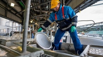 The photo shows a person working in an industrial plant, standing on top of a tanker truck.