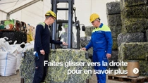 Deux hommes portant des casques jaunes et une salopette de travail se tiennent à côté d’un grand bloc pressé de déchets textiles.&nbsp;