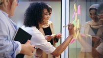 Female office employee writes down on Post its on a glass wall