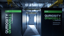 View into the server room of 'Quriosity', BASF's supercomputer at the Ludwigshafen site. Large black server cabinets with the green 'Quriosity' branding line a corridor, illuminated by accent lighting, showcasing BASF's high-performance computing infrastructure for research and development.