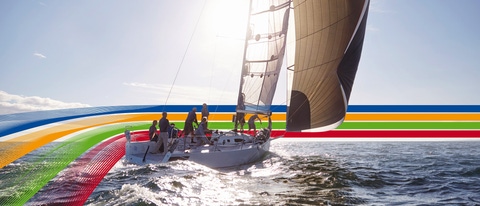 People on a sailing boat in the ocean, under a bright sky, surrounded by a key visual of four lines in blue, orange, green and red (photoshopped)