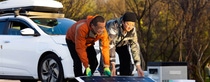 Two men standing in fornt of a white car folding up a custom-build solar panels to charge EVs.
