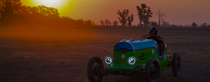 A man sitting in an electric vehicle on a field by sunset. A man sitting in an electric vehicle on a field by sunset.