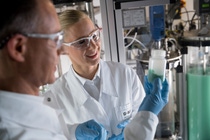 A man and a woman wearing protective goggles stand in a laboratory. A man and a woman wearing protective goggles stand in a laboratory.