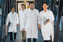 A group of scientists in lab coats walk through a modern corridor.