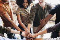 A diverse group of people put their hands over each other with motivation.