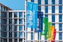 BASF flags in different colors wave in front of a modern office building, displaying the company name and slogan “We create chemistry".