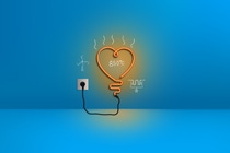 The picture shows an orange neon light in the form of a heart plugged into a blue wall. There are white sketches around it of a wind turbine, an electric heating element and the number “850°C”.