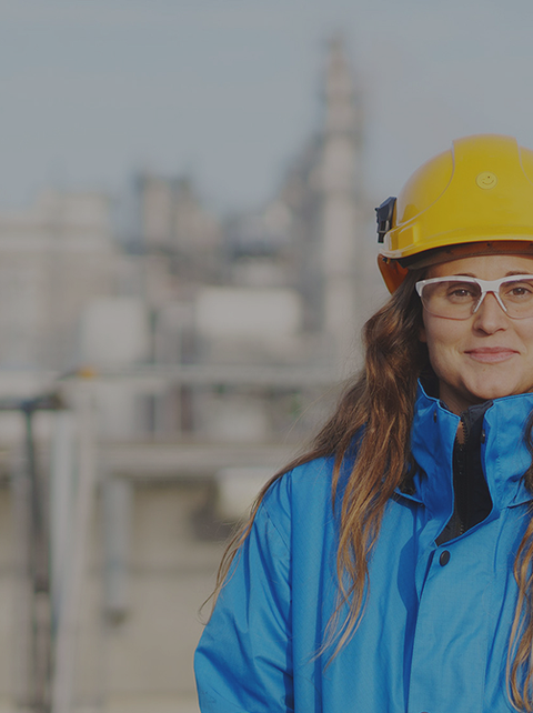 Eine Ingenieurin mit Schutzhelm und Schutzbrille steht vor einer Industrieanlage. Sie arbeitet an nachhaltigen chemischen Innovationen.