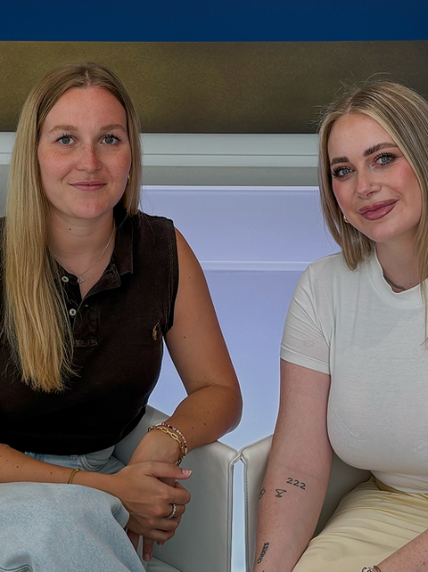 Alena Wolf und Tamara Rettig sitzen auf weißen Sesseln in modernem Raum mit großem Wandbild im Hintergrund