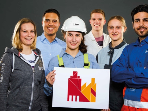 6 Azubis in Arbeitskleidung halten das Key Visual der BASF Münster 6 Azubis in Arbeitskleidung halten das Key Visual der BASF Münster