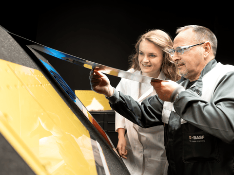 Zwei Mitarbeitende begutachten ein lackiertes Blech Zwei Mitarbeitende begutachten ein lackiertes Blech