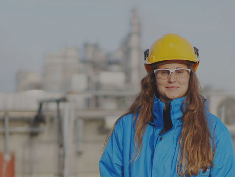An engineer wearing a hard hat and safety goggles stands in front of an industrial plant. She is working on sustainable chemical innovations. An engineer wearing a hard hat and safety goggles stands in front of an industrial plant. She is working on sustainable chemical innovations.