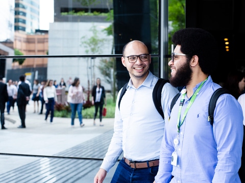 Two BASF employees walk and talk outside a modern office building, smiling as they head to work. Other colleagues can be seen in the background.