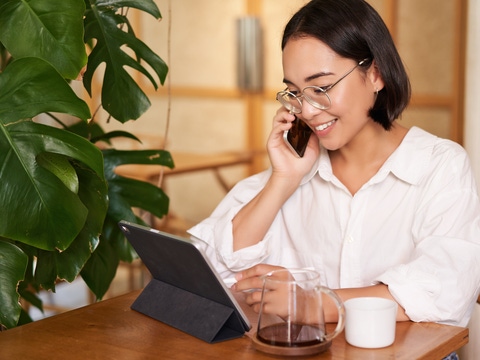 Woman in glasses, answer phone call in a cafe, drinking coffee, looking at work on tablet, working on remote from restaurant.