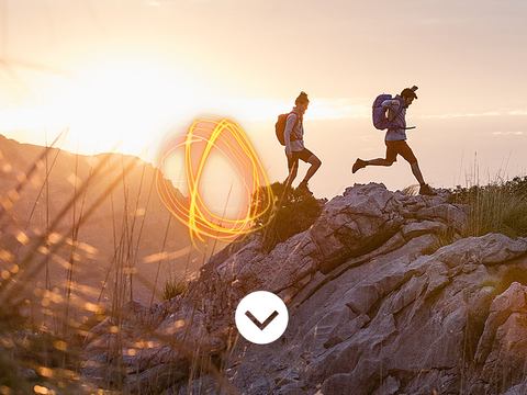 Two people wearing VAUDE backpacks run across rocky terrain in a mountain landscape at sunset. An orange light swirl is visible in the foreground. Two people wearing VAUDE backpacks run across rocky terrain in a mountain landscape at sunset. An orange light swirl is visible in the foreground.