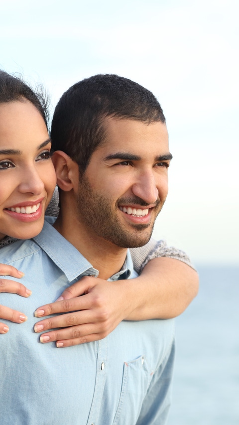 Arab couple flirting piggyback in love on the beach with the sea in the background