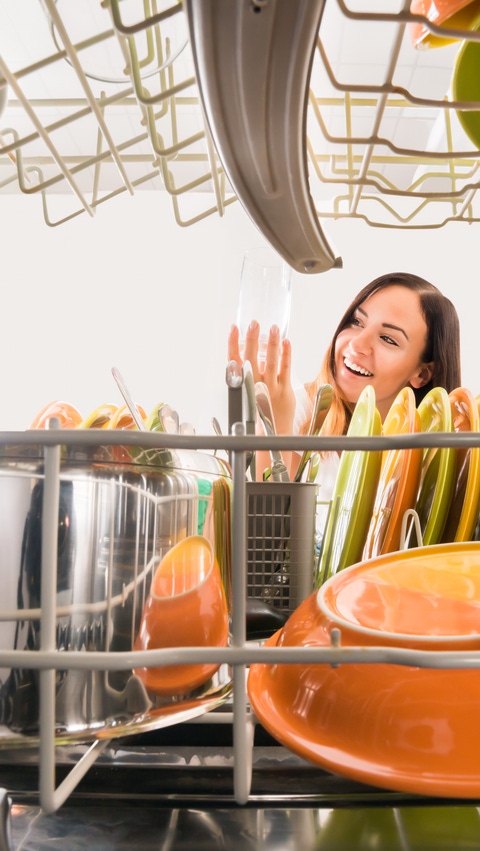 A young woman is taking a clean glass out of a dish washer. A young woman is taking a clean glass out of a dish washer.