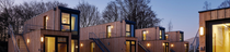A small village of wooden-cladded tiny houses with large windows made from upcycled shipping containers stacked one on top of another. It is dusk and warm-colored lights are illuminating the interiors. (Photo: Stefan Hohloch for Containerwerk) A small village of wooden-cladded tiny houses with large windows made from upcycled shipping containers stacked one on top of another. It is dusk and warm-colored lights are illuminating the interiors. (Photo: Stefan Hohloch for Containerwerk)