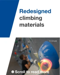 Close-up of a blue climbing hold on an indoor wall, with a climber blurred in the background. 