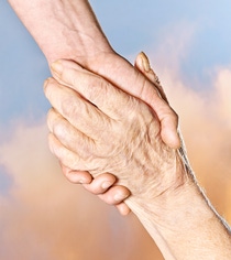 Two hands holding each other tightly, one younger and one older