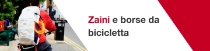 Una persona vista da dietro in bicicletta indossa uno zaino bianco con i loghi VAUDE e BASF e un anello luminoso arancione. Il testo recita: «Zaini e borse da bicicletta.»