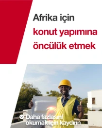 Sarı bir güvenlik yeleği ve baret giyen bir adam bir binanın önünde ayakta duruyor ve elinde bir inşaat karosu tutuyorMetinde şunlar yazıyor: “Afrika için öncü konut.”