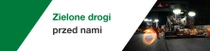 Budowa drogi w nocy z udziałem pracowników i maszyn. Nad sceną unosi się świetlny wir. Tekst brzmi: „Przed nami bardziej ekologiczne drogi”.