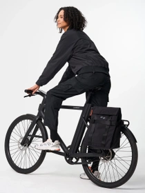 Person riding a bicycle with a black bicycle bag on the rear rack. 