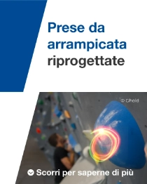 Primo piano di una presa di arrampicata blu su una parete interna, con uno scalatore sfocato sullo sfondo.