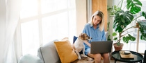 Women working on laptop with dog beside her in her living room. Women working on laptop with dog beside her in her living room.