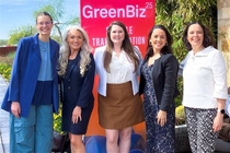 A group of five people standing in front of a red banner with the text 'GreenBiz 25 THE TRANSITION' written on it. The individuals are dressed in business casual attire and are posing for a photo outdoors, with greenery and plants visible in the background. A group of five people standing in front of a red banner with the text 'GreenBiz 25 THE TRANSITION' written on it. The individuals are dressed in business casual attire and are posing for a photo outdoors, with greenery and plants visible in the background.