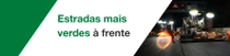 Uma construção de estrada à noite com trabalhadores e máquinas. Um redemoinho de luz paira sobre a cena. O texto diz: “Estradas mais verdes à frente”.