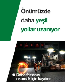 Gece işçiler ve makinelerle yapılan bir yol inşaatı. Metinde şunlar yazıyor: “Gelecekte daha yeşil yollar.”