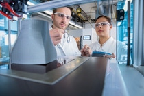 At the Application Technology Center in Heidelberg, Germany, BASF tests new powders, resins, filaments and granulates for 3D printing and develops solutions for industrial additive manufacturing. Alexander Gengel, application technician 3D printing, takes a finished printed part out of a 3D printer. Also pictured: Fernanda Kraft, application technician 3D printing