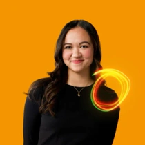 A female BASF employee stands in a black top in front of an orange background. A red-green light swirl hovers in front of her chest.