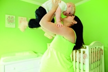 Pregnant woman lifting son (2-4) in air in nursery, smiling, side view Pregnant woman lifting son (2-4) in air in nursery, smiling, side view