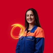 A female BASF employee in an orange and blue work overall standing against a red background, a light swirl hovers around her shoulder.  