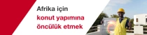 Sarı bir güvenlik yeleği ve baret giyen bir adam bir binanın önünde ayakta duruyor ve elinde bir inşaat karosu tutuyorMetinde şunlar yazıyor: “Afrika için öncü konut.”