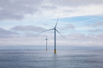 A wind farm under construction. Two wind turbines in a blue ocean. In the backdrop, you can find three more monopile foundations and a ship. A wind farm under construction. Two wind turbines in a blue ocean. In the backdrop, you can find three more monopile foundations and a ship.